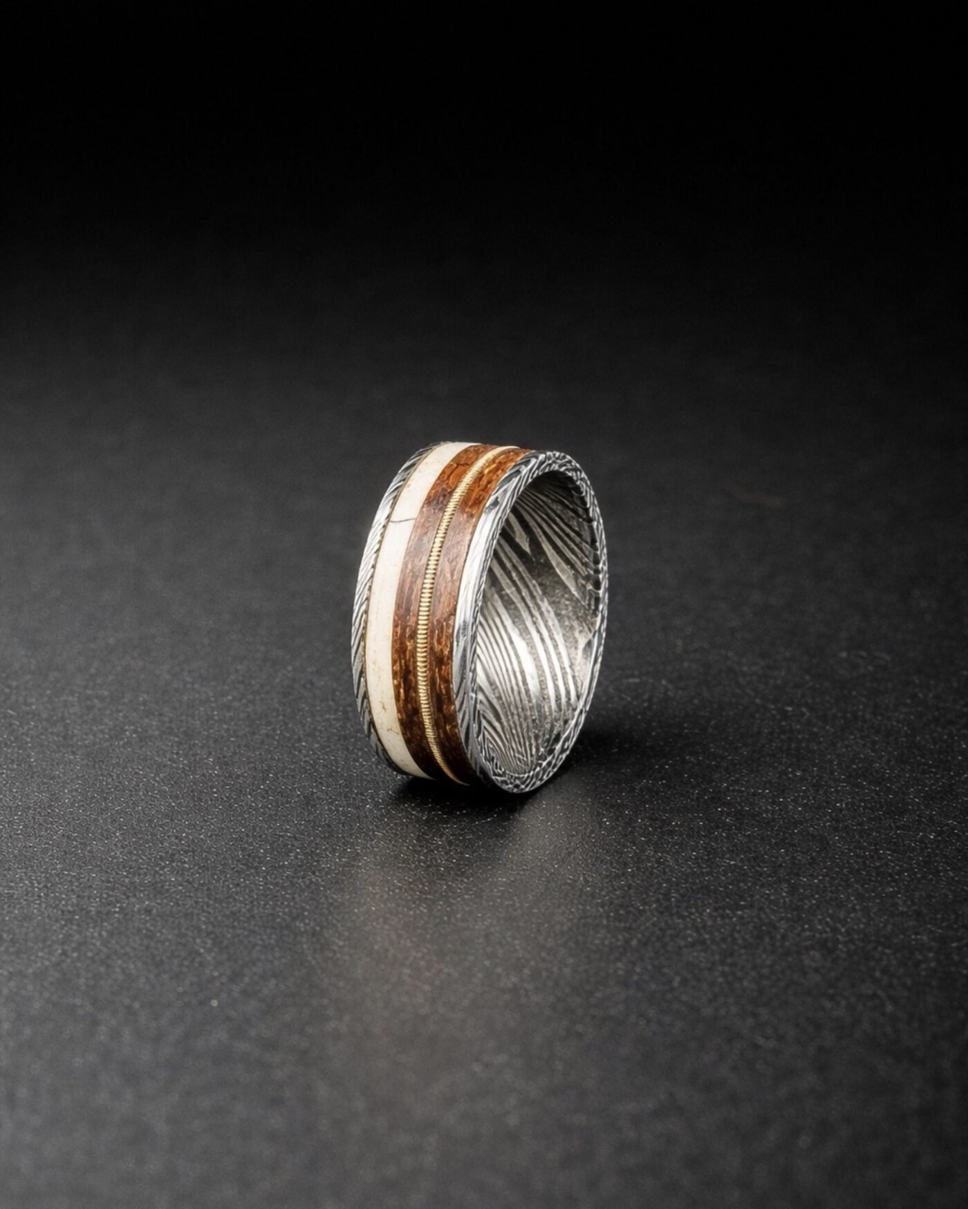 The finished ring photographed on a dark surface, the coiled guitar string visible in the channel.