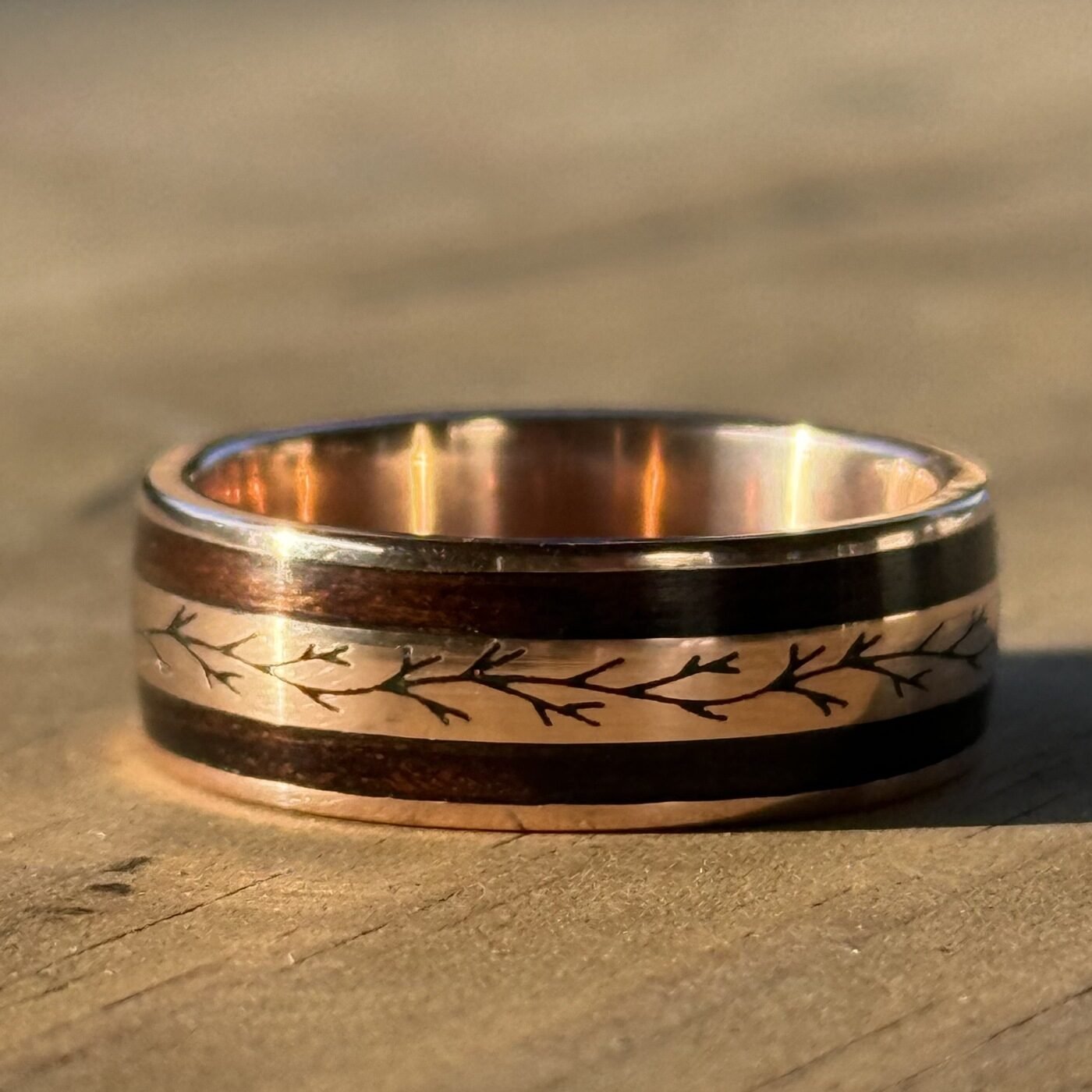 The finished band on a wooden bench, the engraved branch catching the light.